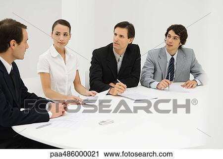 Team of professionals sitting together at table, discussing, looking at each other View Large Photo Image Stock Image - Team of professionals sitting together at table, discussing, looking at each other. Fotosearch