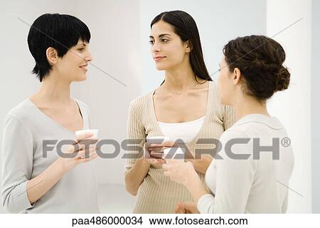 Three businesswomen chatting together, holding hot beverages View Large Photo Image Picture - Three businesswomen chatting together, holding hot beverages. Fotosearch