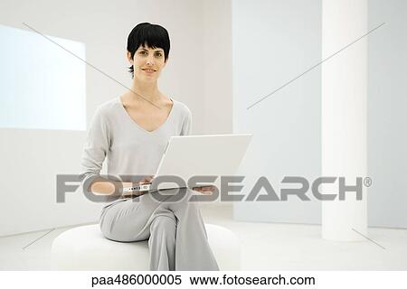 Woman sitting, holding laptop computer, smiling at camera View Large Photo Image Stock Photography - Woman sitting, holding laptop computer, smiling at camera. Fotosearch