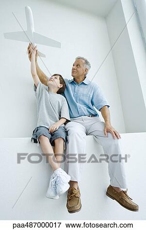 Grandfather and grandson sitting side by side, holding up toy airplane together View Large Photo Image Stock Photo - Grandfather and grandson sitting side by side, holding up toy airplane together. Fotosearch