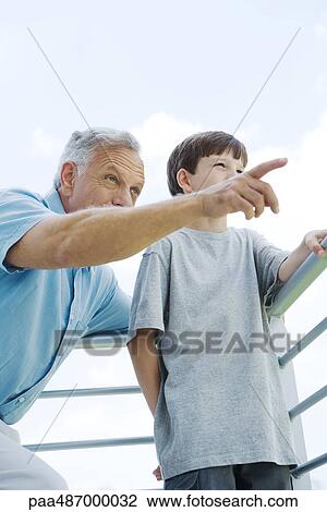 Grandfather and grandson standing by railing together, man pointing, both looking away View Large Photo Image Stock Image - Grandfather and grandson standing by railing together, man pointing, both looking away. Fotosearch