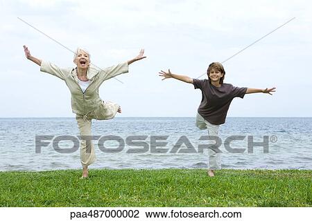 Grandmother and grandson standing on one leg, arms outstretched, both smiling at camera View Large Photo Image Stock Image - Grandmother and grandson standing on one leg, arms outstretched, both smiling at camera. Fotosearch