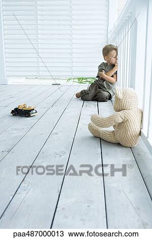 Stock Image - Little boy sitting on porch with arms folded, leaning against railing, looking away. Fotosearch