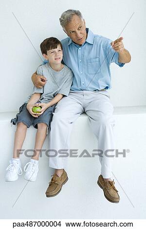 Man sitting with arm around grandson's shoulders, pointing, both looking away View Large Photo Image Picture - Man sitting with arm around grandson's shoulders, pointing, both looking away. Fotosearch