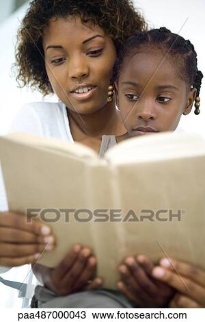 Stock Image - Mother and daughter reading book together, girl sitting on woman's lap, close-up. Fotosearch