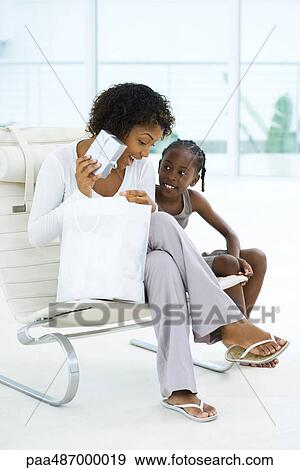 Mother sitting next to daughter, holding up gift, both smiling View Large Photo Image Stock Photo - Mother sitting next to daughter, holding up gift, both smiling. Fotosearch
