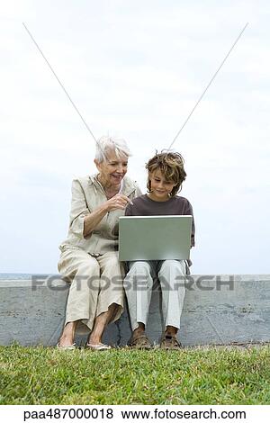 Stock Photo - Senior woman and grandson sitting outdoors, using laptop computer together. Fotosearch