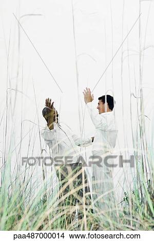 Two men greeting each other outdoors, hands raised, viewed through tall grass View Large Photo Image Picture - Two men greeting each other outdoors, hands raised, viewed through tall grass. Fotosearch