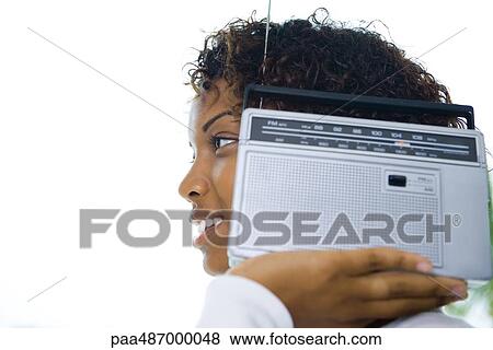 Stock Photo - Woman holding radio next to ear, smiling, side view. Fotosearch