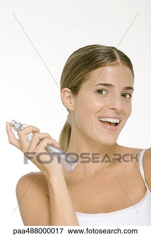 Stock Photo - Woman holding up bottle of perfume, smiling at camera. Fotosearch