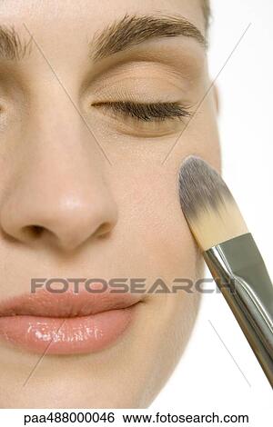 Stock Photograph - Woman putting on blush, smiling with eyes closed, close-up of face. Fotosearch