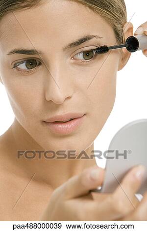 Woman putting on mascara, looking in hand mirror, close-up View Large Photo Image Stock Photo - Woman putting on mascara, looking in hand mirror, close-up. Fotosearch