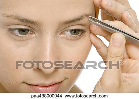 Picture - Woman using tweezers to pluck eyebrows, close-up. Fotosearch