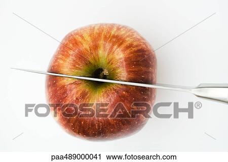 Stock Image - Knife cutting apple in half, high angle view, close-up. Fotosearch