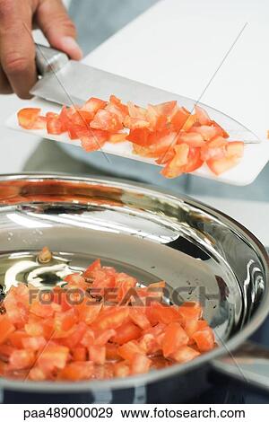 Stock Photo - Man scraping diced tomatoes into saucepan with knife, cropped view. Fotosearch