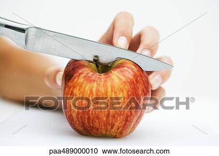 Stock Image - Woman cutting apple with knife, cropped view of hand. Fotosearch