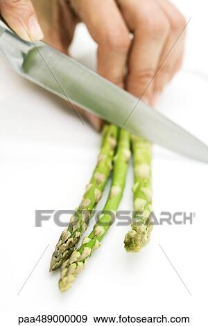 Stock Photo - Woman cutting asparagus with knife, cropped view of hand. Fotosearch