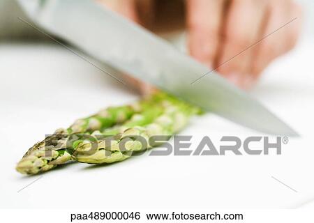 Stock Photograph - Woman cutting asparagus with knife, close-up cropped view. Fotosearch