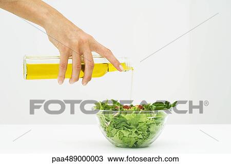 Stock Image - Woman pouring olive oil on salad, cropped view of hand. Fotosearch