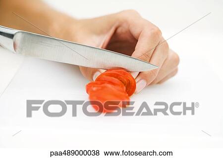 Stock Photo - Woman slicing tomato with knife, cropped view of hand. Fotosearch