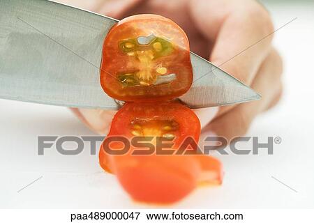 Stock Photo - Woman slicing tomato with knife, cropped view of hand. Fotosearch