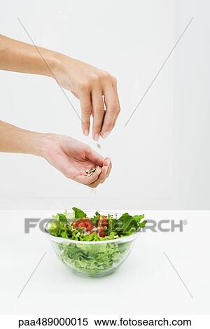 Stock Photography - Woman sprinkling sunflower seeds on salad, cropped view of hands. Fotosearch