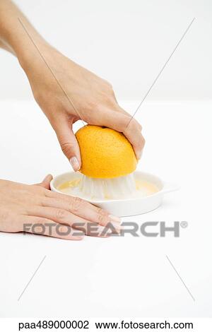 Stock Image - Woman squeezing orange with citrus press, cropped view of hands. Fotosearch