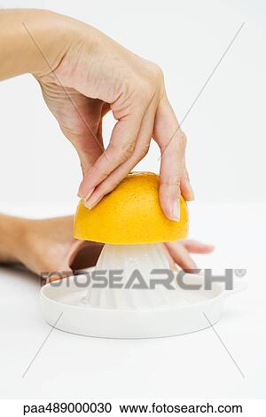 Stock Image - Woman squeezing orange with citrus press, cropped view of hands. Fotosearch