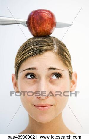 Stock Image - Young woman apple and knife on head, close-up. Fotosearch