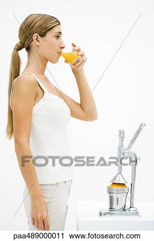 Young woman standing in front of citrus press, drinking freshly squeezed orange juice View Large Photo Image Stock Image - Young woman standing in front of citrus press, drinking freshly squeezed orange juice. Fotosearch