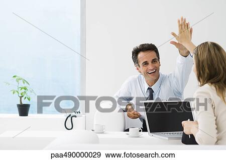 Stock Photo - Business associates giving each other high-five in office. Fotosearch