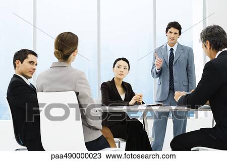 Business associates having meeting, one standing, pointing View Large Photo Image Stock Image - Business associates having meeting, one standing, pointing. Fotosearch
