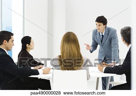 Stock Photo - Business associates having meeting, manager leaning on table, pointing. Fotosearch