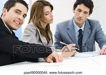 Business associates reading document, businessman in foreground, holding pen, smiling at camera View Large Photo Image Stock Photography - Business associates reading document, businessman in foreground, holding pen, smiling at camera. Fotosearch