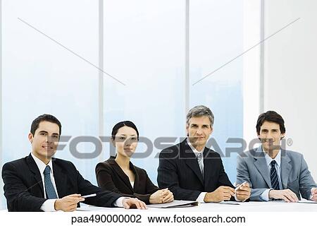 Stock Image - Business associates sitting at meeting table, smiling at camera. Fotosearch