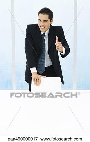 Businessman leaning on back of chair, giving thumbs up to camera View Large Photo Image Stock Photo - Businessman leaning on back of chair, giving thumbs up to camera. Fotosearch