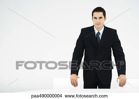 Picture - Businessman leaning on backs of chairs, looking at camera. Fotosearch