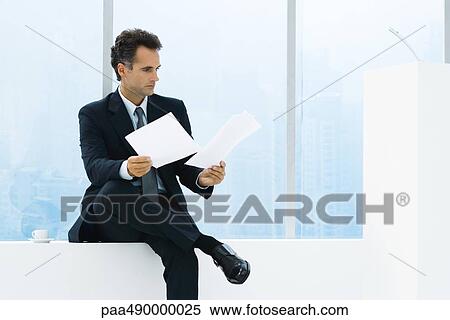 Stock Photography - Businessman sitting by window, studying documents. Fotosearch