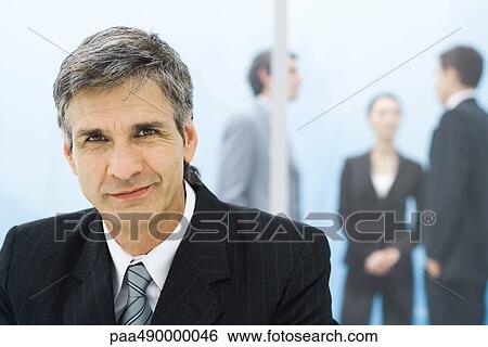 Stock Photograph - Businessman smiling at camera, colleagues in background. Fotosearch