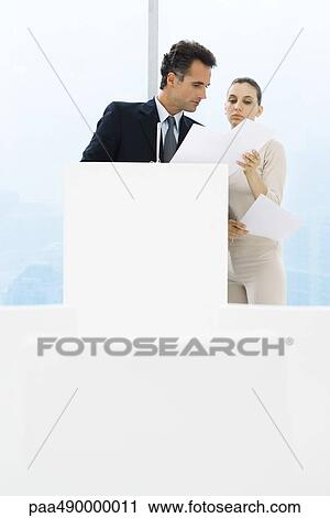 Businessman standing by lectern, female assistant holding up documents for him View Large Photo Image Stock Image - Businessman standing by lectern, female assistant holding up documents for him. Fotosearch