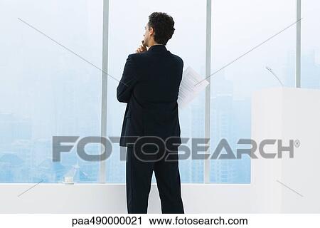 Businessman standing by window, holding document under arm, thinking, rear view View Large Photo Image Stock Image - Businessman standing by window, holding document under arm, thinking, rear view. Fotosearch