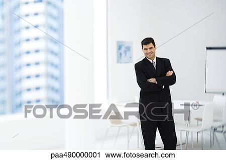 Businessman standing in meeting room with arms crossed, smiling at camera View Large Photo Image Stock Image - Businessman standing in meeting room with arms crossed, smiling at camera. Fotosearch