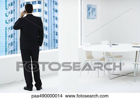 Businessman standing, looking out window, using cell phone View Large Photo Image Picture - Businessman standing, looking out window, using cell phone. Fotosearch