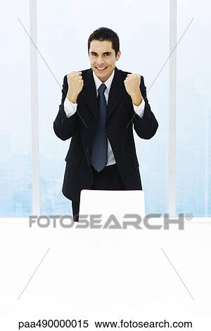 Stock Photography - Businessman standing with fists up, smiling at camera. Fotosearch