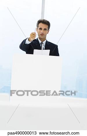 Executive standing behind lectern, pointing with pen at camera View Large Photo Image Stock Image - Executive standing behind lectern, pointing with pen at camera. Fotosearch
