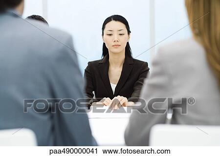 Stock Image - Executives in meeting, focus on businesswoman holding document in background. Fotosearch
