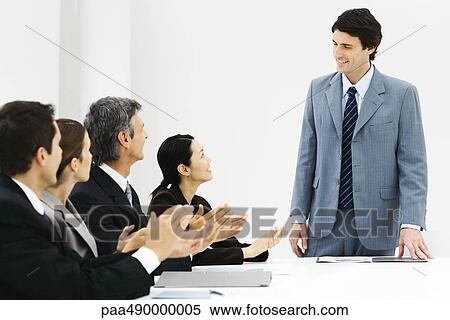 Stock Photography - Group of business associates applauding colleague during meeting. Fotosearch