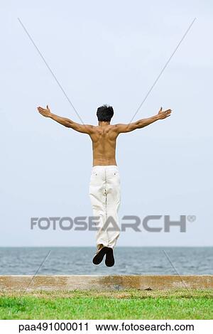 Man jumping in the air at the beach, arms outstretched, rear view View Large Photo Image Stock Image - Man jumping in the air at the beach, arms outstretched, rear view. Fotosearch