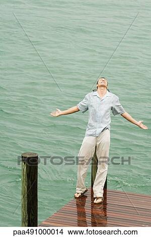 Man leaning back on pier in the rain, arms out, eyes closed, high angle view View Large Photo Image Picture - Man leaning back on pier in the rain, arms out, eyes closed, high angle view. Fotosearch