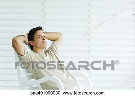 Man sitting in chair with hands behind head, looking away View Large Photo Image Stock Image - Man sitting in chair with hands behind head, looking away. Fotosearch